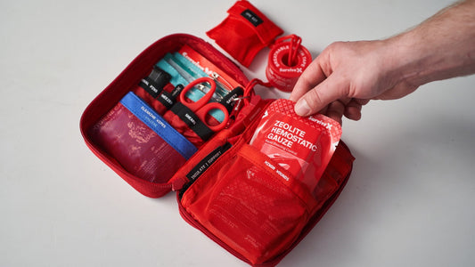 Hand pulling SurviveX Zeolite Hemostatic Gauze from a red first aid kit